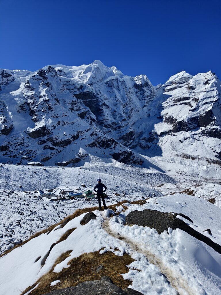 A trekker standing on the edge overlooking huge mountains covered in snow.
