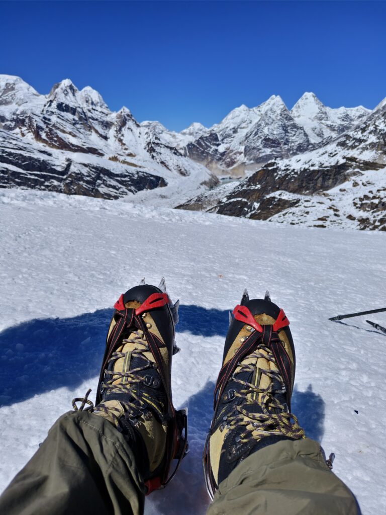 A climber resting on a mountain, climbing boots with crampons facing towards the mountains.